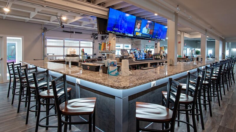 Corner view of bar with many stools and large flat screen tvs above bar